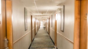 A hotel hallway with a carpeted floor, wooden doors, and framed pictures on the walls. - Travelodge by Wyndham Escanaba (Escanaba)
