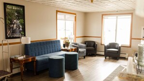 A hotel room with a blue sofa, two ottomans, a grey armchair, a black armchair, a wooden side table, and a poster on the wall. - Travelodge by Wyndham Escanaba (Escanaba)
