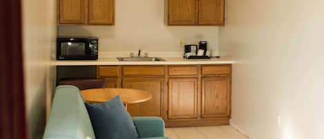 Una cocina compacta con armarios de madera, microondas, cafetera y una pequeña mesa de comedor.