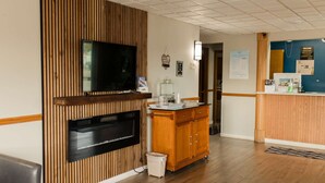 A hotel lobby with a wooden reception desk, a flat-screen TV mounted on a wall, a trash bin, and a seating area with a chair. - Travelodge by Wyndham Escanaba (Escanaba)