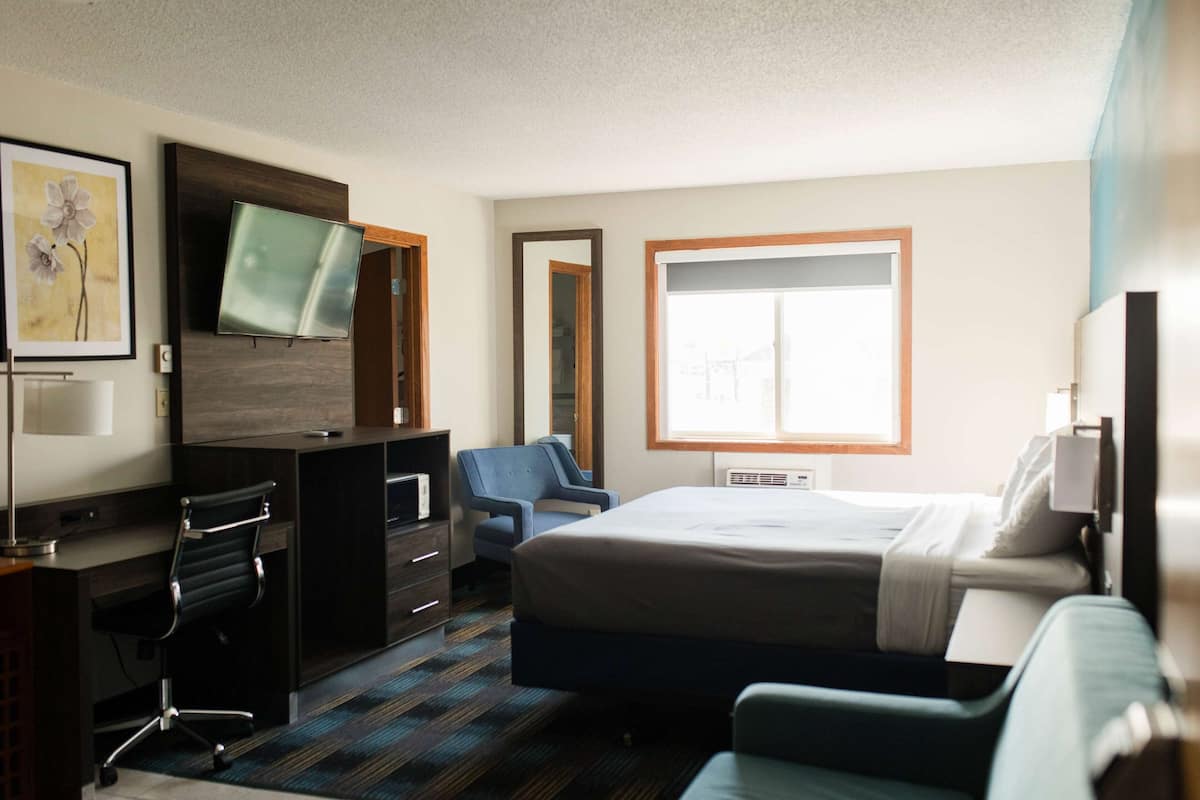 Habitación de hotel con cama, escritorio, silla, televisor y un amplio ventanal.