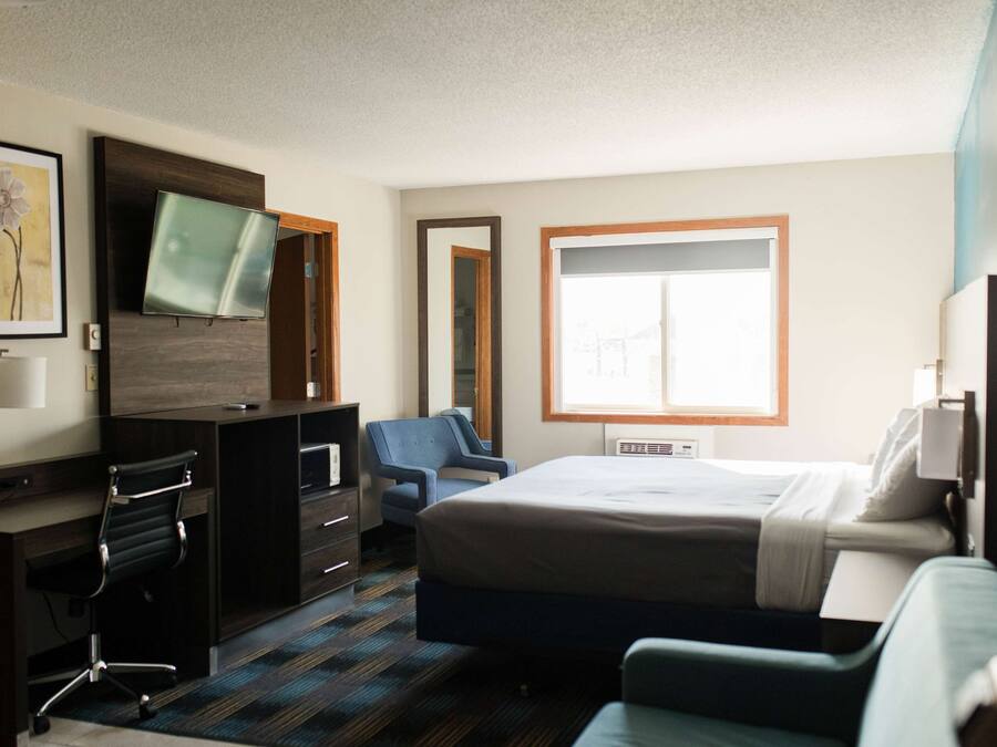 A hotel room with a bed, desk, chair, TV, and a large window.