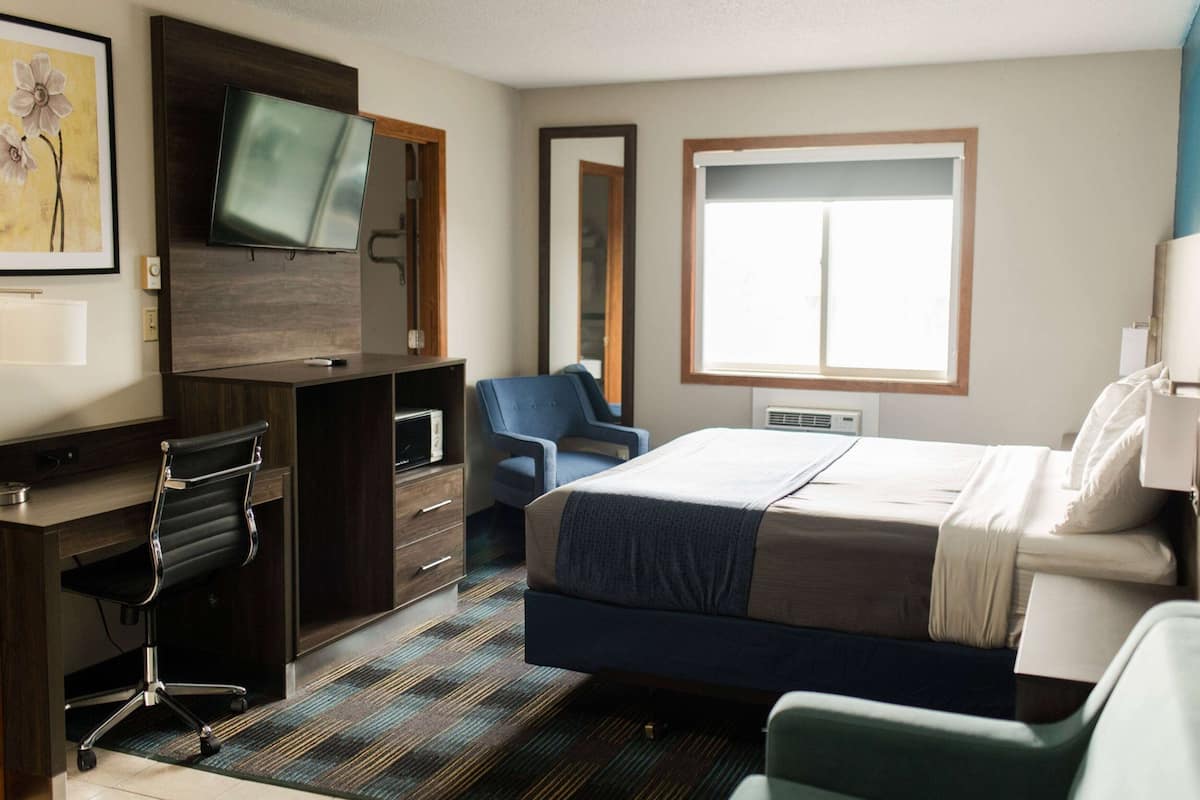 Habitación de hotel con cama, escritorio, silla, televisor y un ventanal grande.