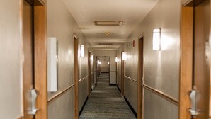 A hotel hallway with carpeted floors, wooden doors, and wall-mounted lights. - Travelodge by Wyndham Escanaba (Escanaba)