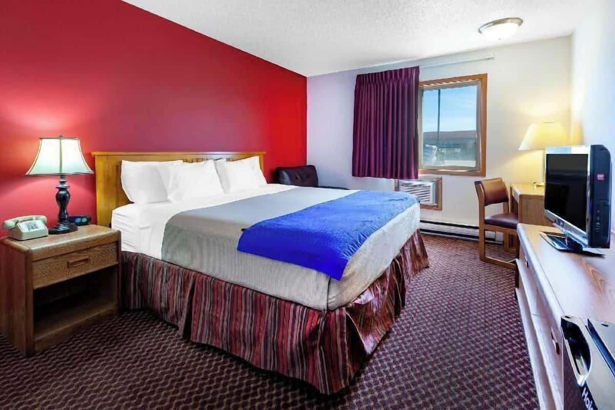 Habitación de hotel con cama, escritorio, televisión, teléfono y ventana con cortinas.