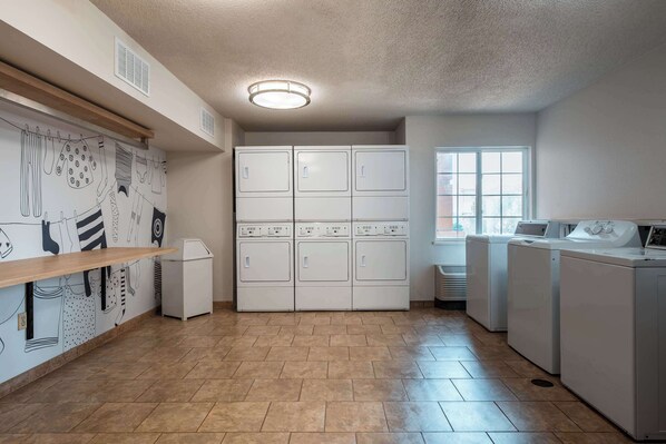 A laundry room with a tiled floor, a drying rack, a wall-mounted drying rack, and a large wall-mounted washer and dryer unit.