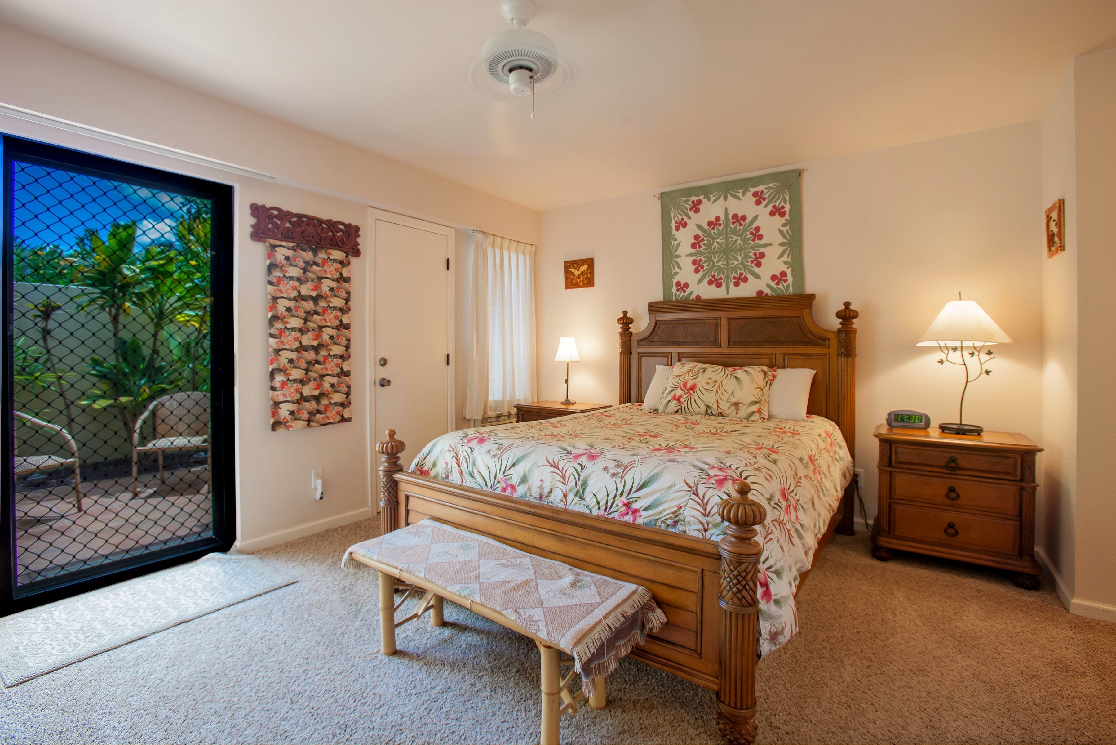 A bedroom with a bed, a bench, a nightstand, a lamp, and a door leading to a balcony.