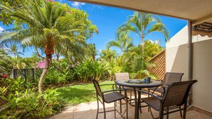 Une terrasse avec une table ronde et des chaises, entourée d’une végétation luxuriante et de palmiers.