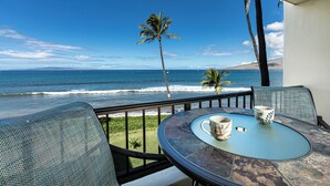 Un balcon avec une table et des chaises donnant sur une plage bordée de palmiers et où l’on peut admirer les vagues de l’océan.