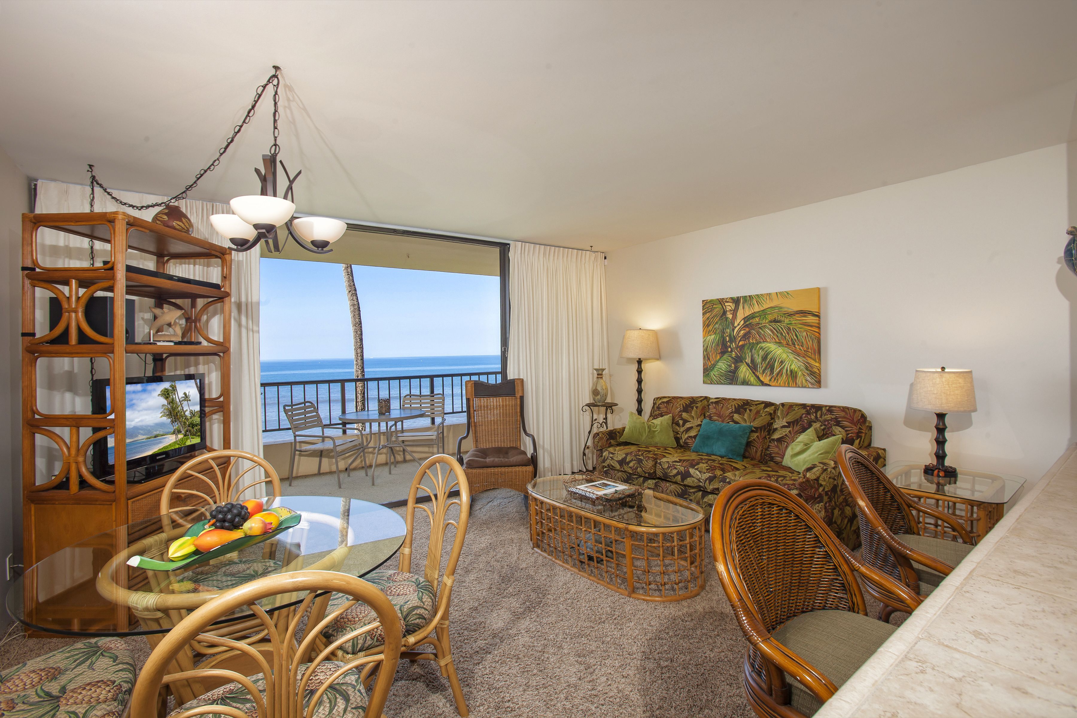A living room with a dining area, wicker furniture, a television, and a view of the ocean.