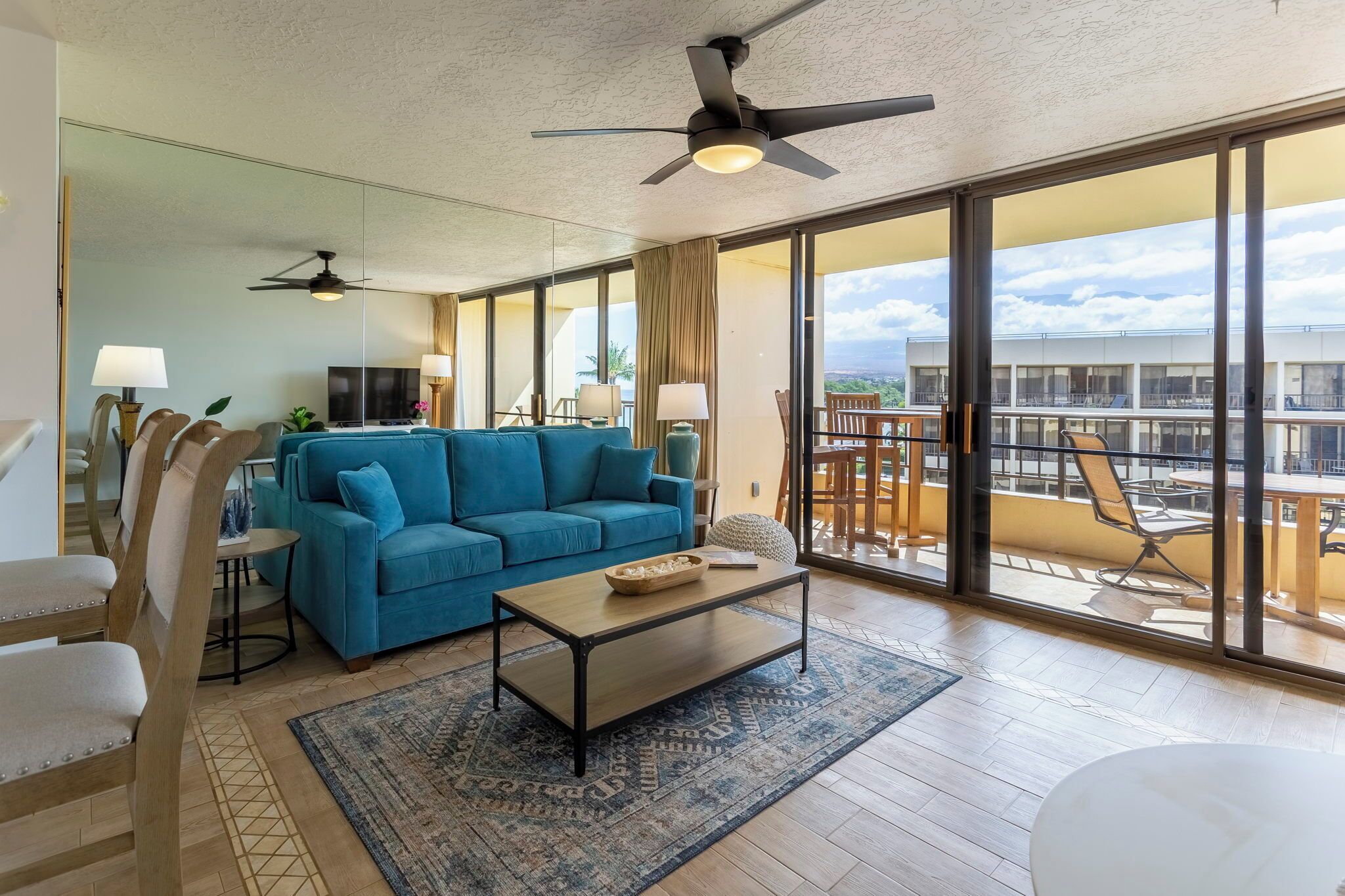Ein geräumiges Wohnzimmer mit blauem Sofa, einem Couchtisch und einem Balkon mit Sitzgelegenheit.