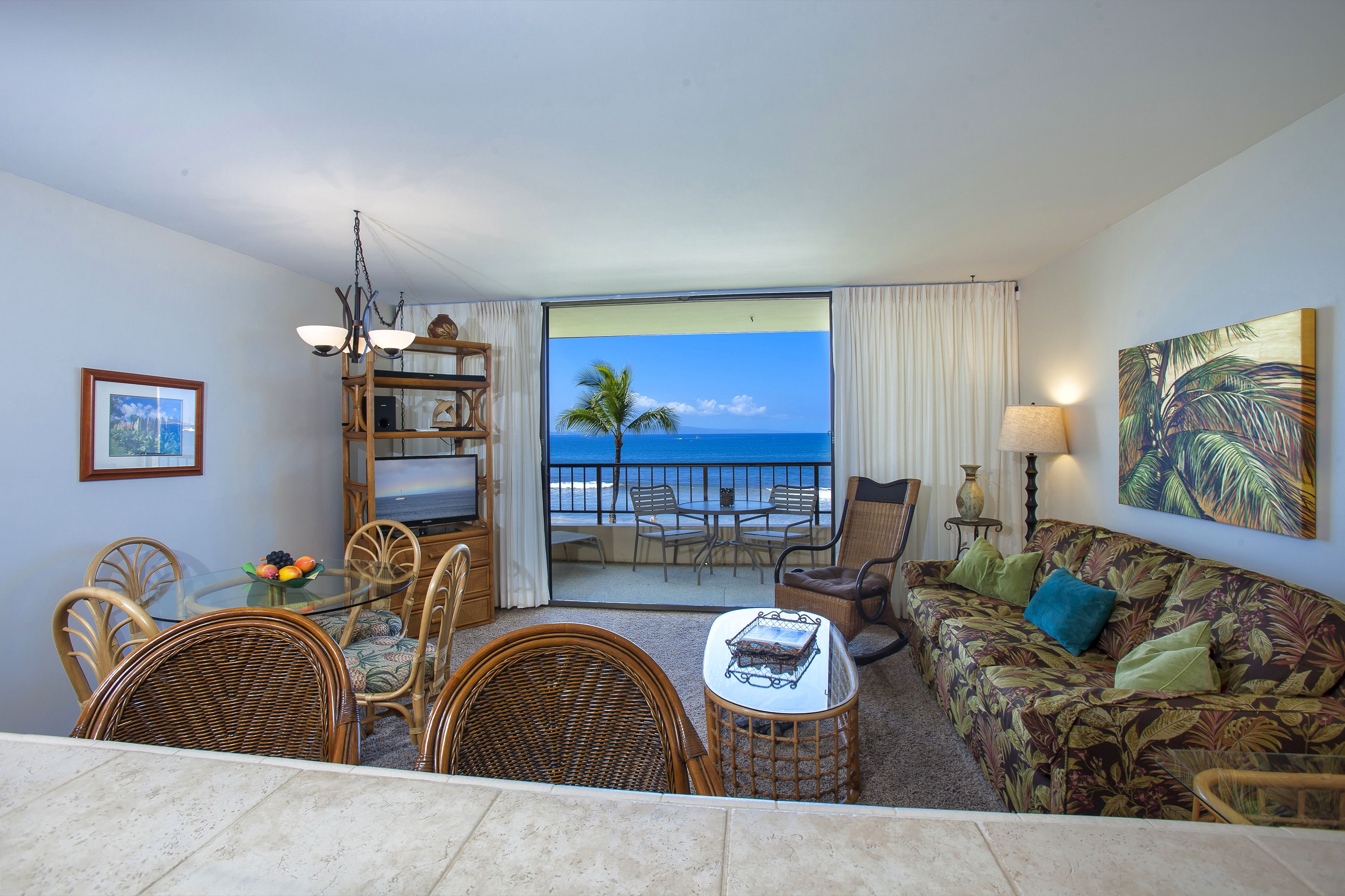 A room with a dining table, chairs, a sofa, and a view of the ocean.