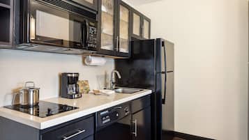 A modern kitchen with black cabinets, a stainless steel refrigerator, a built-in microwave, and a coffee maker.