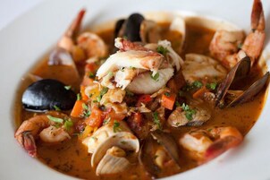 Un plato de mariscos con camarones, mejillones, almejas y un trozo de pescado, adornado con hierbas.