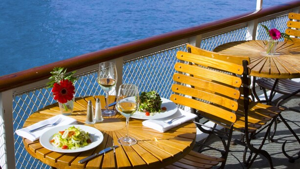 A dining table with a plate of food, a glass of white wine, and a vase with flowers on a ship deck. - Delta King Hotel (Sacramento)