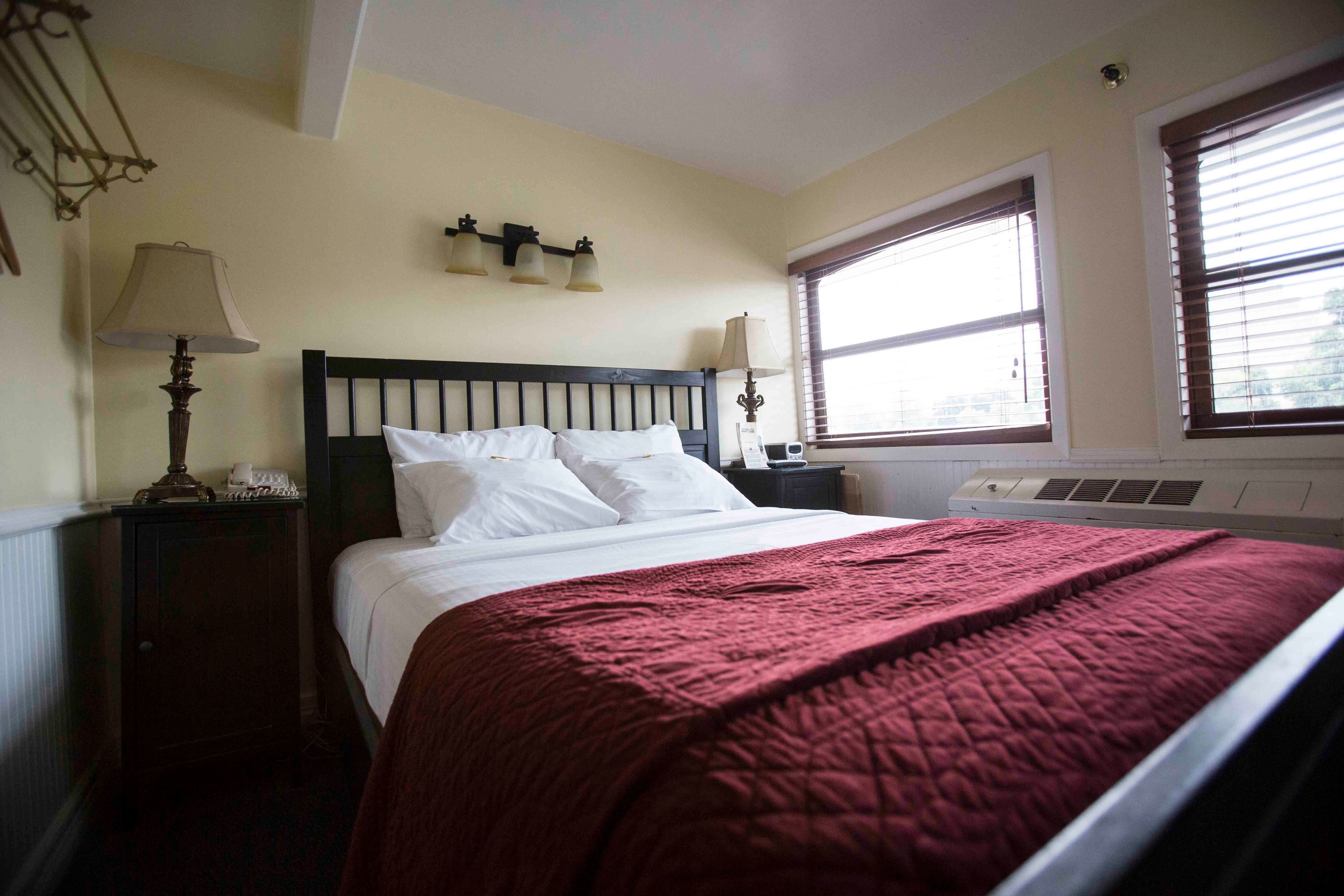 Une chambre à coucher comprenant un lit, une table de chevet, une lampe, une fenêtre et un luminaire fixé au mur.