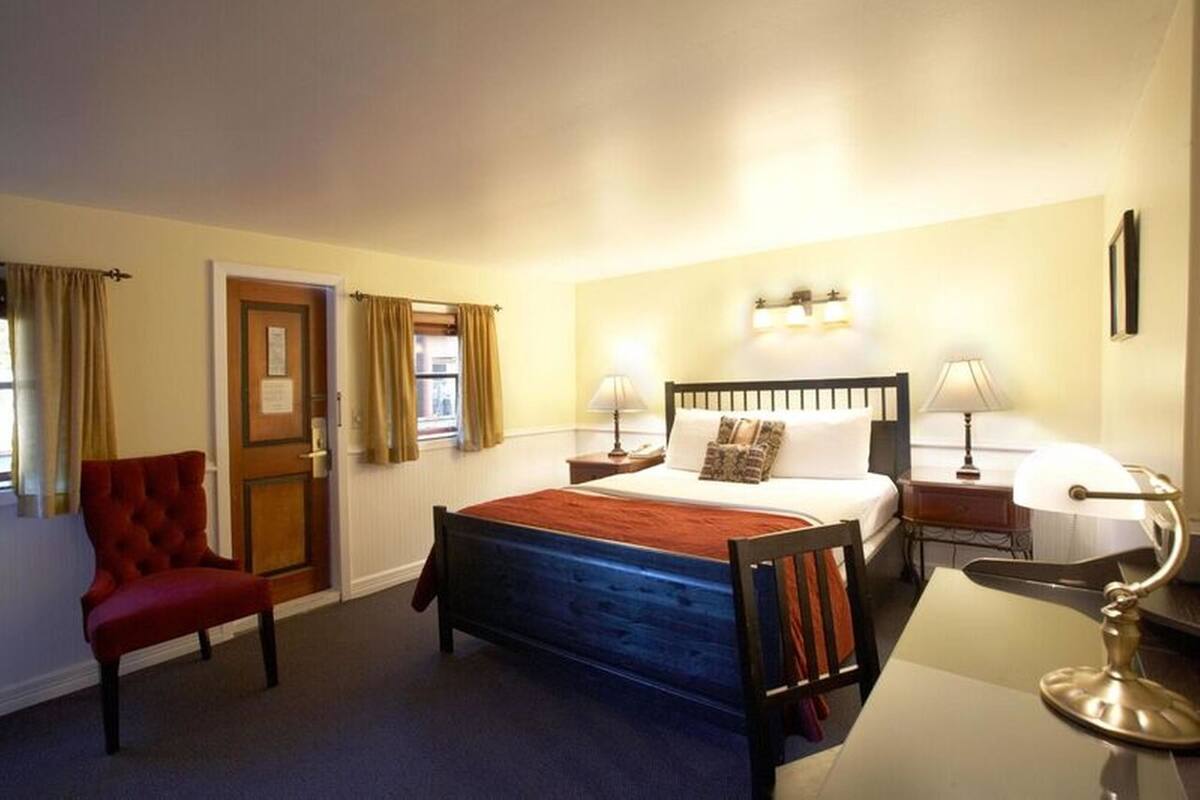 A hotel room with a bed, a desk, a chair, and a door.