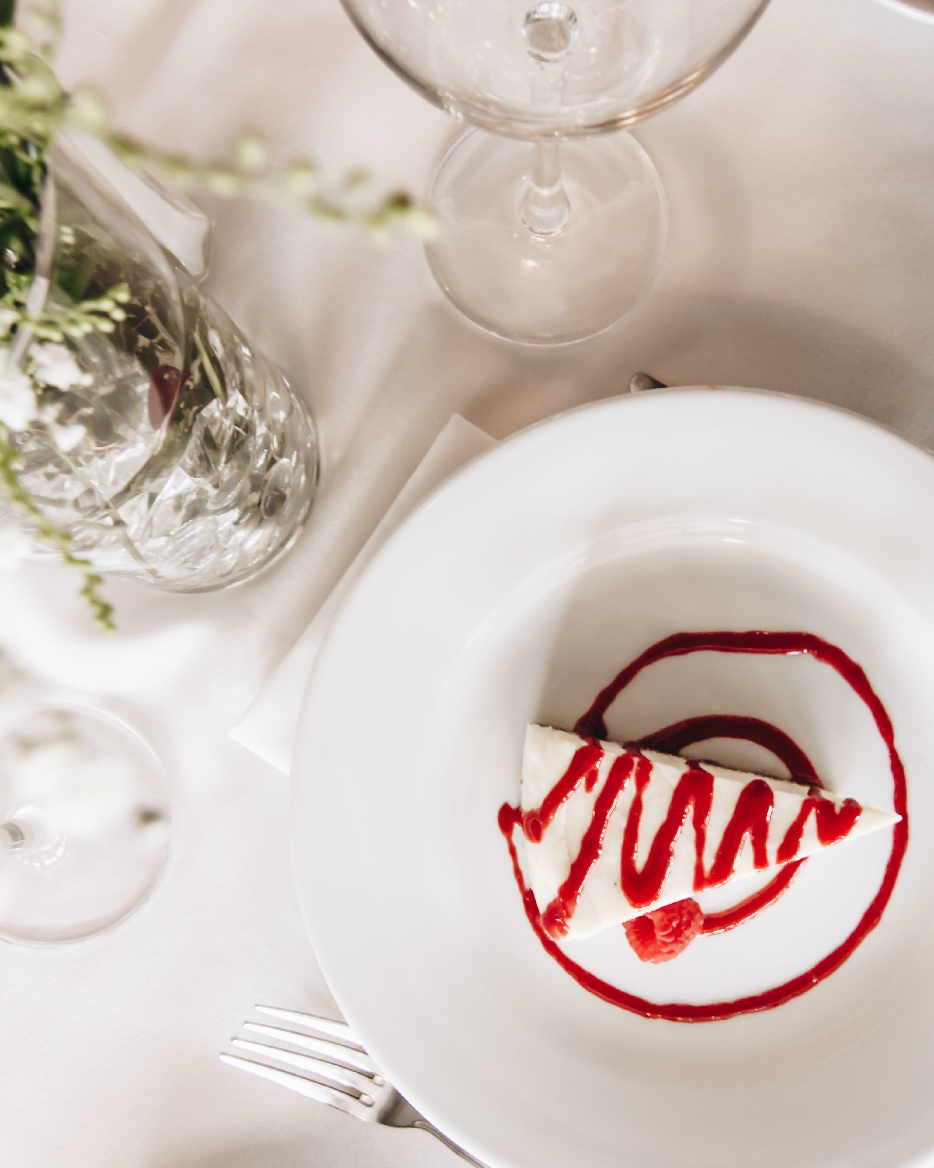 A dessert on a white plate with a red garnish, a fork, and a glass of water on a table.