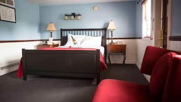 A hotel room with a bed, two bedside tables, a red chair, and a window with blinds.