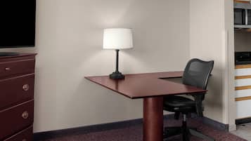 A conference room with a desk, chair, lamp, and a television on a dresser.