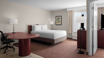 A hotel room with a bed, a desk, a chair, a lamp, a picture on the wall, and a window with curtains.
