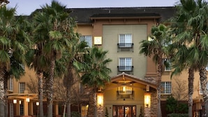 A multi-story hotel with a central entrance, palm trees, and a warm exterior lighting.