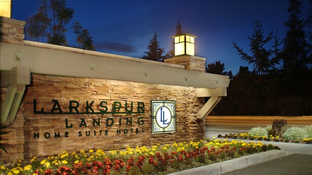 A stone facade with a sign for Larkspur Landing Home Suite Hotel, a lantern, and a flower bed.