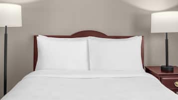Una cama bien hecha con sábanas blancas, un cabecero de madera y dos lámparas de noche a cada lado.