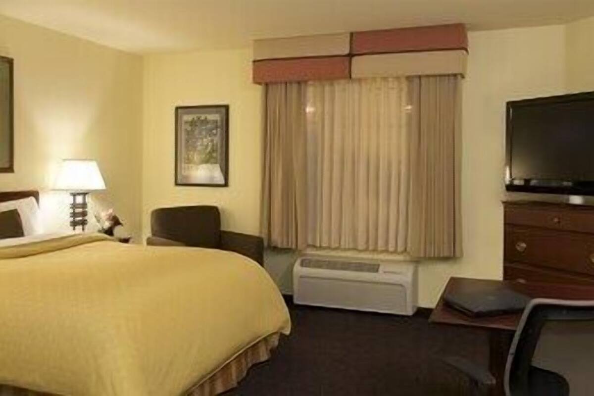 Ein Hotelzimmer mit Bett, Schreibtisch, Stuhl, Fernseher und einem Fenster mit Vorhängen.
