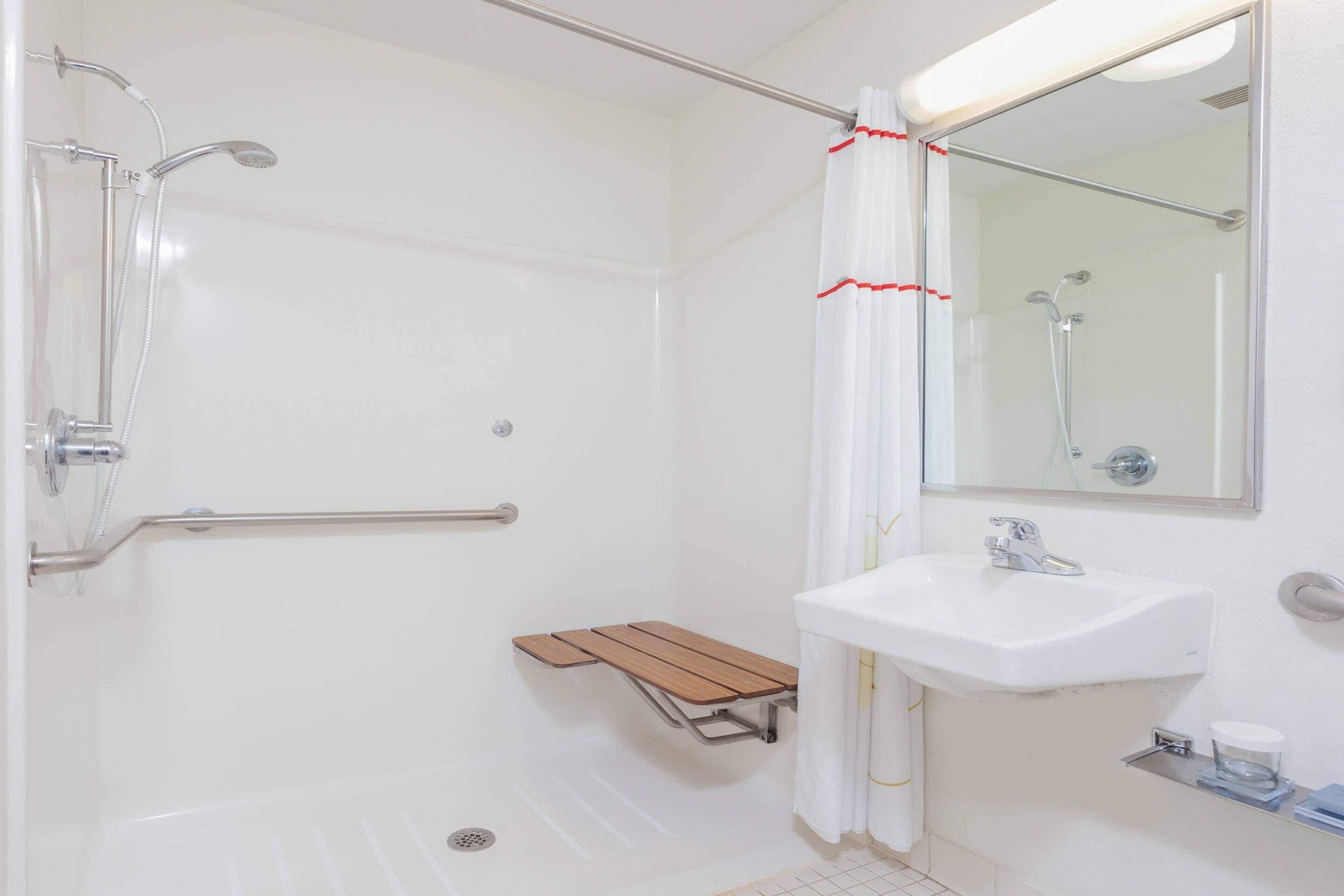 Une salle de bain avec une douche, un lavabo, un miroir et un banc en bois.