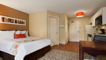 Quarto de hotel com cama, escrivaninha e cozinha compacta.