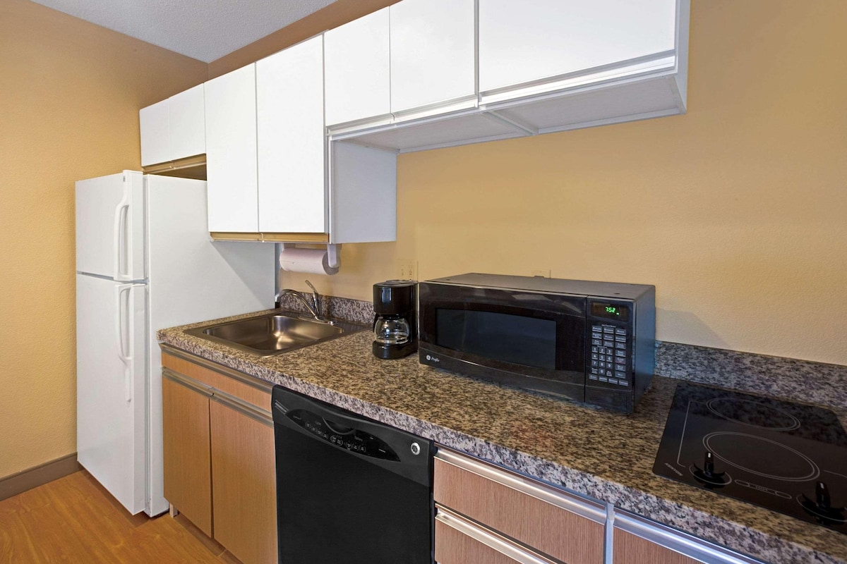 A compact kitchen with white cabinets, a stainless steel sink, a black microwave, and a dishwasher.