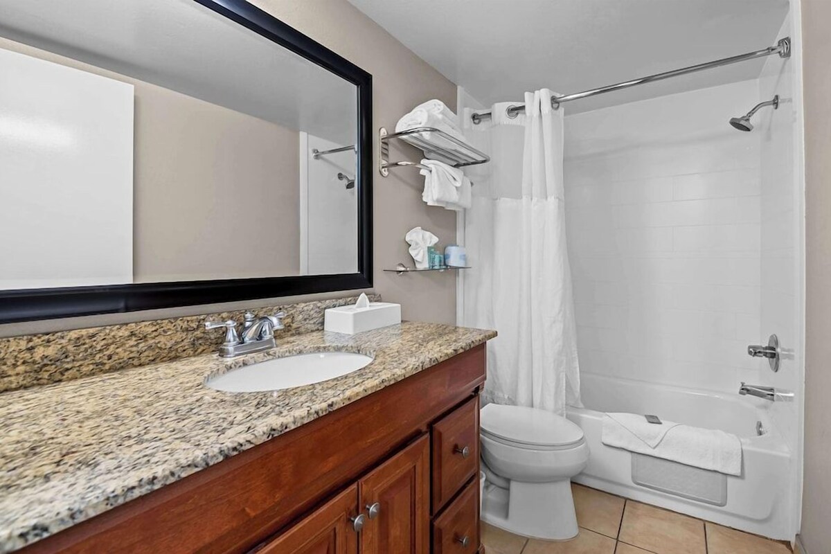 A bathroom with a granite countertop sink, a mirror, a toilet, and a shower with a glass door.