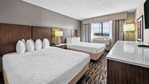 Habitación de hotel con dos camas, un escritorio, una lámpara y un ventanal con vistas.