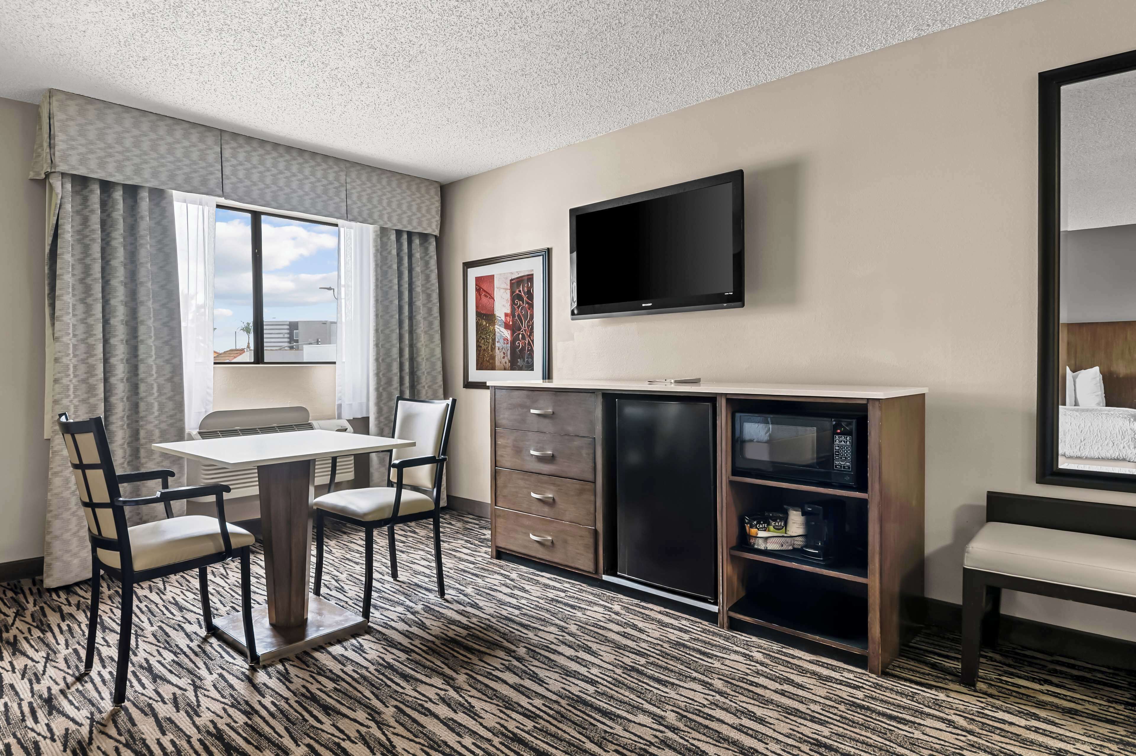 A hotel room with a dining table, chairs, a TV, a minibar, and a window with curtains.