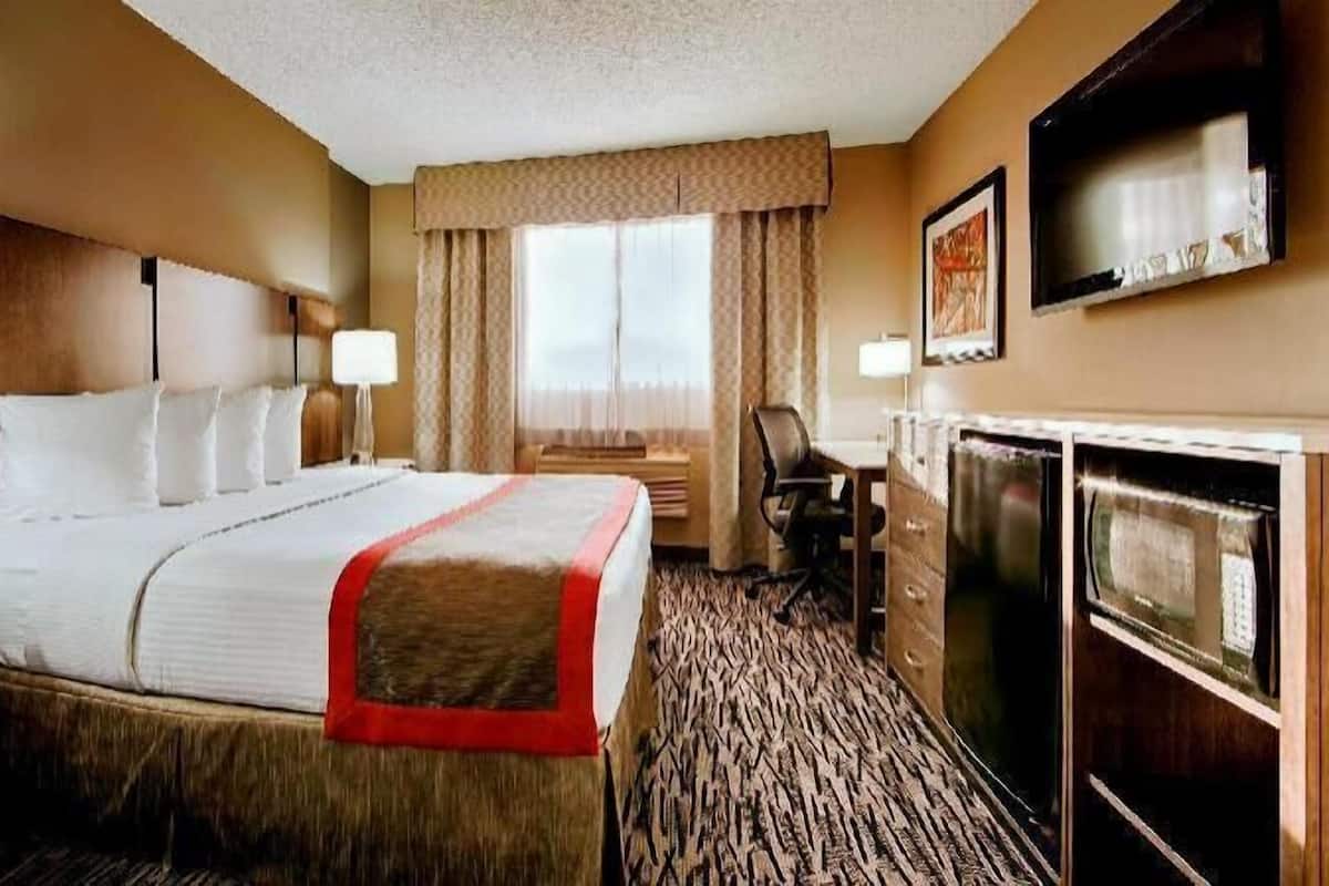 A hotel room with a bed, desk, chair, television, and a window with curtains.