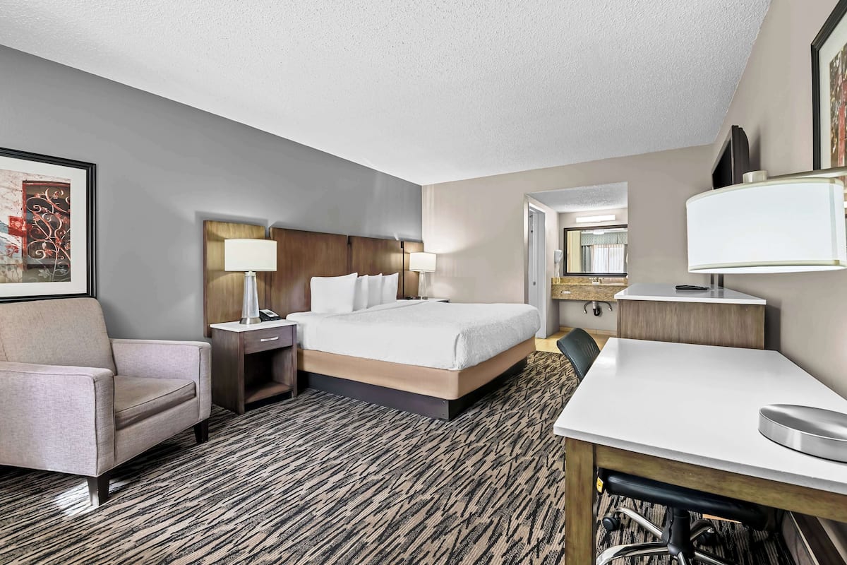 A hotel room with a bed, a desk, a chair, a nightstand, and a lamp.