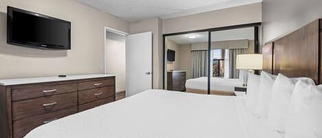 A hotel room with a large bed, a flat-screen TV mounted on the wall, a wooden dresser, and a sliding glass door leading to a balcony.