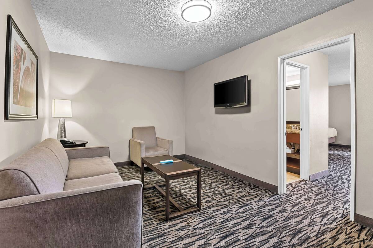 A hotel room with a sofa, a small table, a TV, and a patterned carpet.