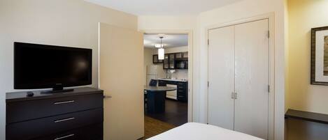 A hotel room with a bed, a TV on a dresser, a kitchenette, and a dining area.