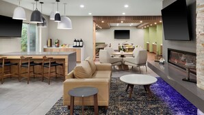 Ein modernes Wohnzimmer mit einer Couch, einem Couchtisch und einem Essbereich. Ein Kamin und ein Flachbildfernseher an der Wand sind vorhanden.