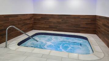 A rectangular hot tub with a metal faucet, surrounded by white tiles and a wooden accent wall.
