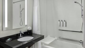 Un baño moderno con lavamanos de encimera negra, un espejo, ducha con cabezal de ducha manual y barra de apoyo.