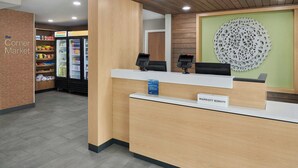 Ein Hotel-Empfangsbereich mit einem hölzernen Empfangstresen, einer großen Wanddekoration und einer Kühlvitrine im Hintergrund.