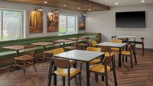 Ein Restaurant mit Holztischen und -stühlen, einer gepolsterten grünen Bank und Bildern an den Wänden.