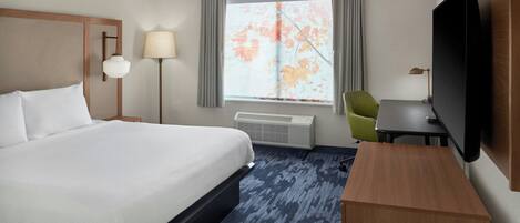 A hotel room with a large bed, a desk, a television, a lamp, and a window with curtains.
