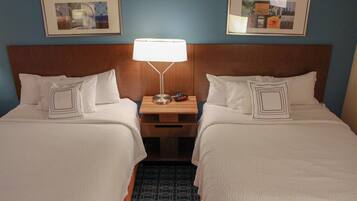 A hotel room with two beds, a nightstand with a lamp, and framed pictures on the wall.