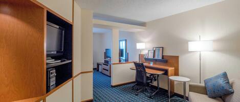 A hotel room with a kitchenette, a desk with a computer, a sofa, and a small table.