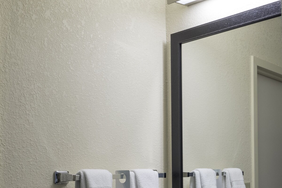 A bathroom with a white sink, a mirror, and three white towels hanging on a towel rack.