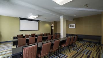 A conference room with a large table, chairs, a projector screen, and carpeted flooring.
